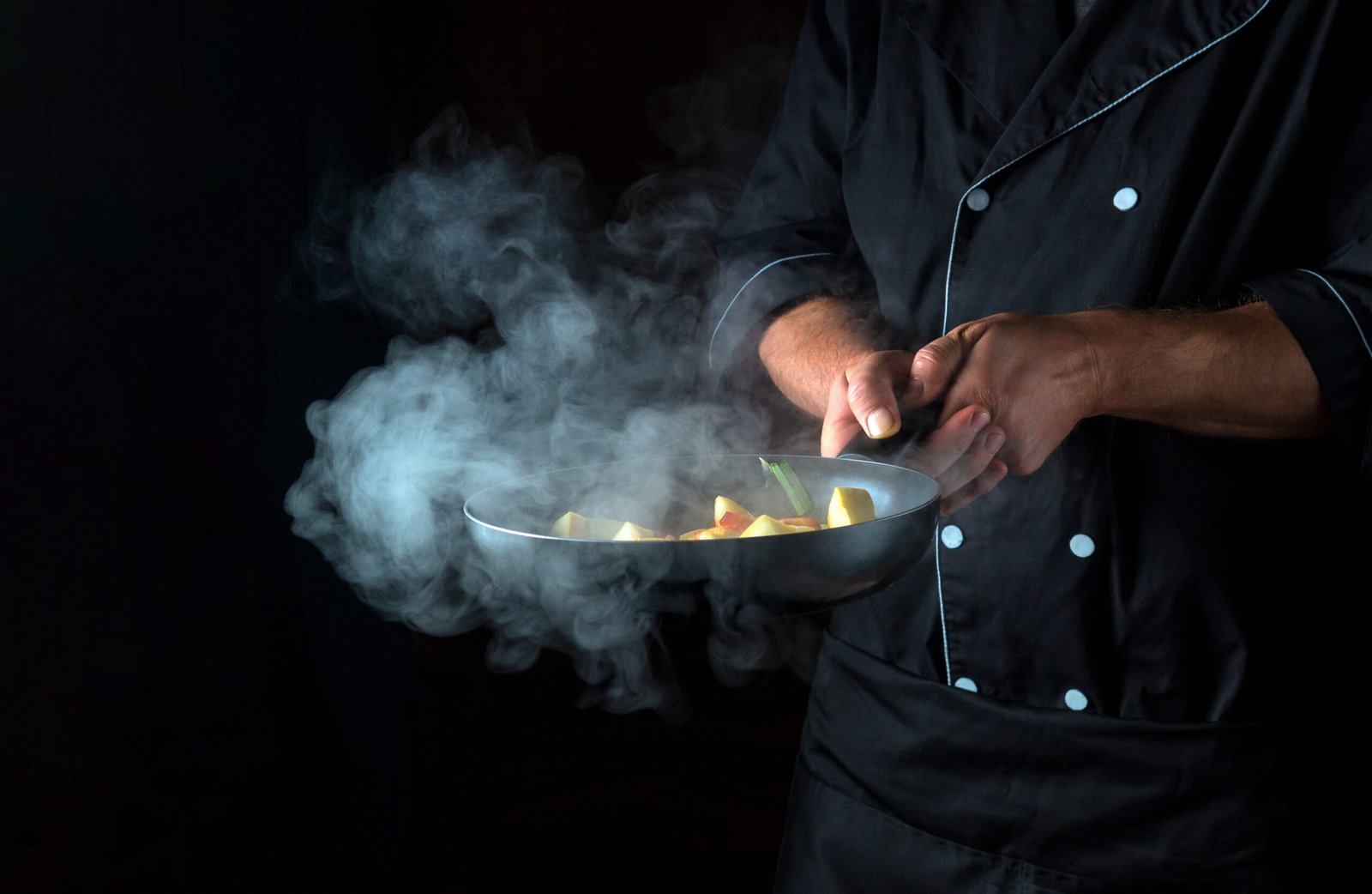 Professional chef prepares vegetables in a frying pan. Cooking healthy vegetarian food and meal on a dark background. Free advertising space.